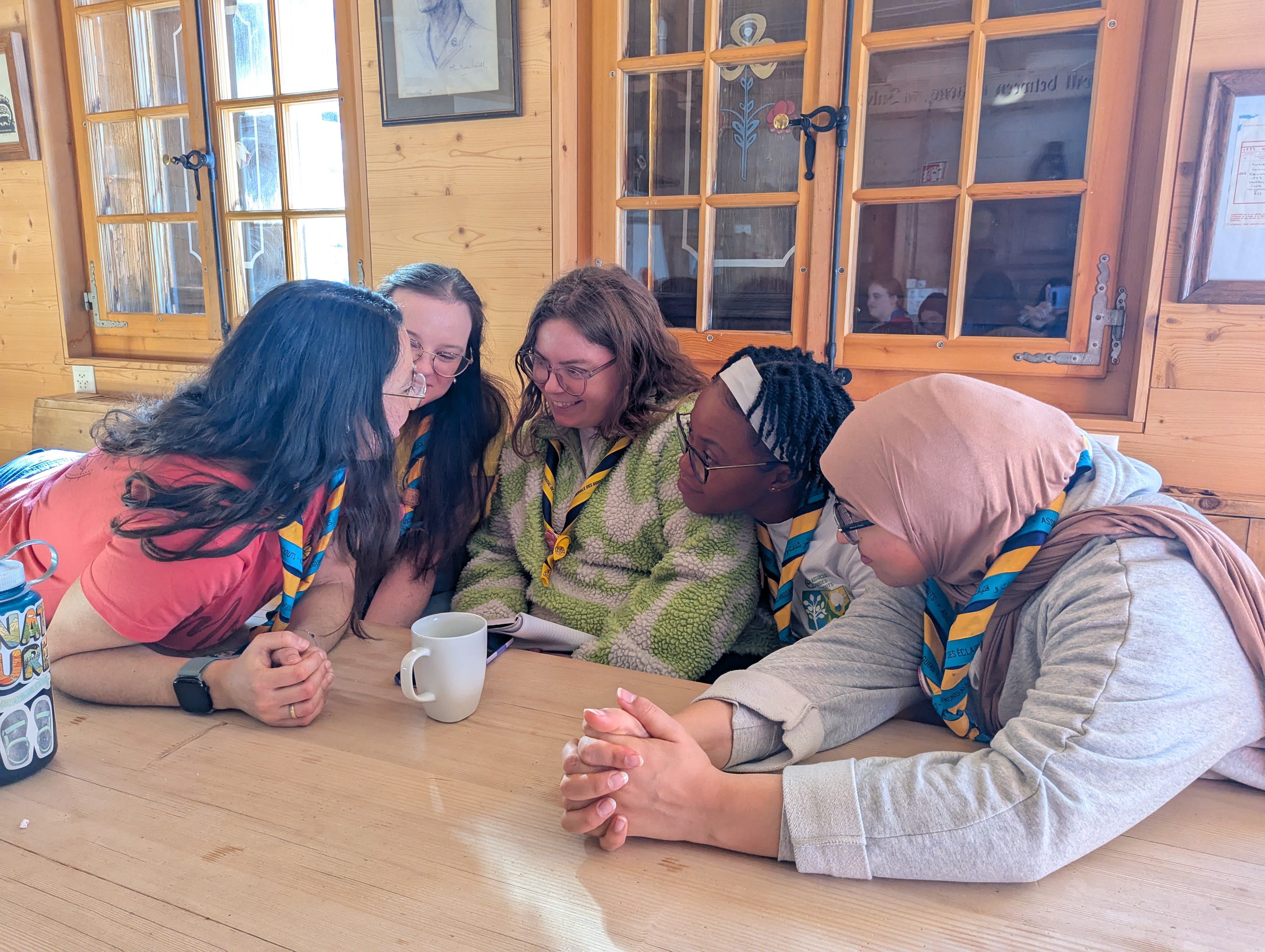 group of young women who are volunteering as facilitators at Our Chalet, huddled around a table having a discussion