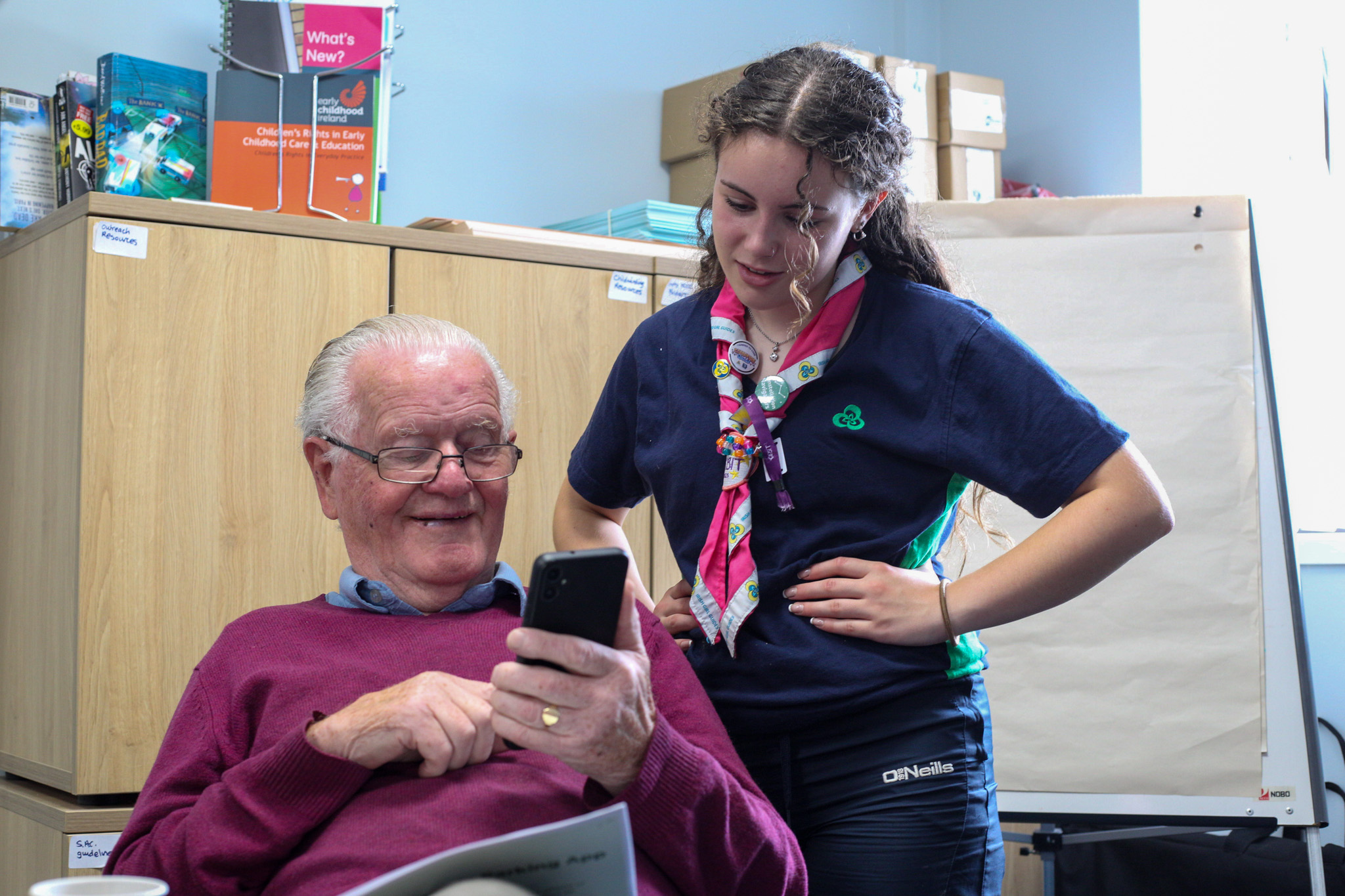 image of Irish Girl Guide helping member of Kildare Men's Shed use a mobile phone