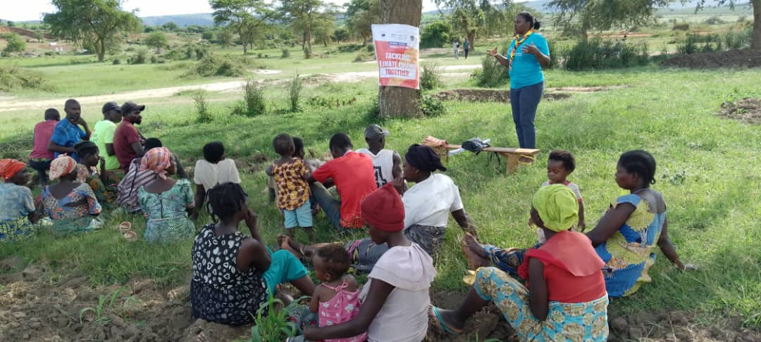 Nelly standing, facilitating to a group of children, young people and their parents sitting and listening. 