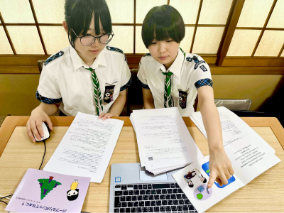 image of two Girl Scouts from Japan working on a book and pointing at a laptop screen